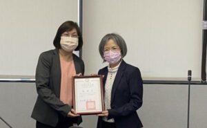 兩名女性於室內空間合影，兩人共同手持感謝狀，呈現頒贈與致意的情形。