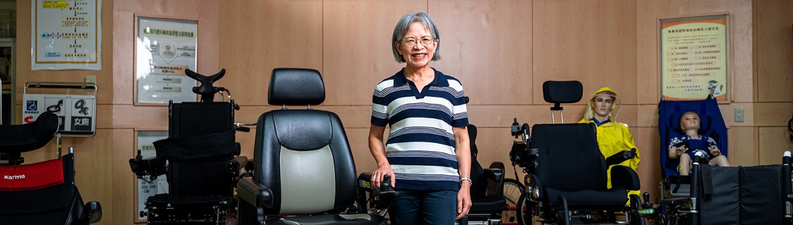 中心主任站於輔助科技研究中心大廳中，周圍陳列多項輔具設備。